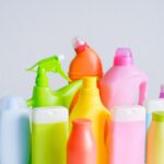 Composition of different colorful plastic containers with detergents for disinfect and daily routine placed on table against white background in room
